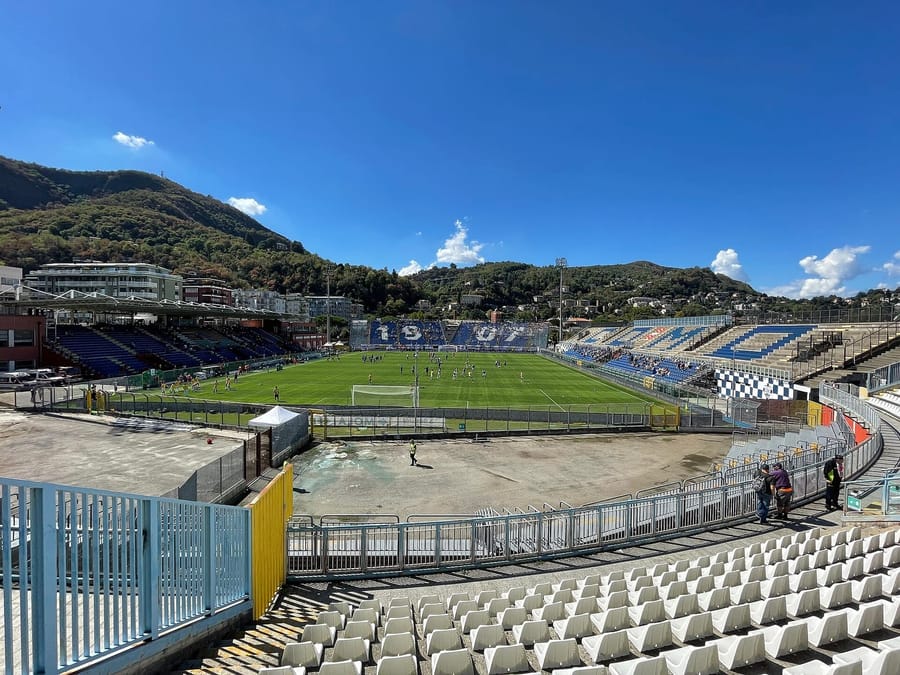 View from the stands of Como's Stadio Giuseppe Sinigaglia, with the end stand spelling out 1907 and players warming up on the pitch